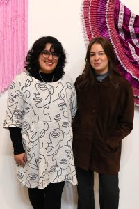 Stephani Trujillo and Talia Belen Laing in front of their collaborative pieces La Sangre Llama and Marinera skirt, 2024 - Ni de Aqui Ni de Alla (photo by Saranne Carrasco-Brennan)